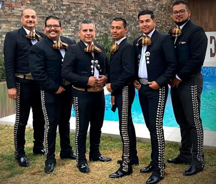 Seis de los músicos de Mariachi Internacional, de pie, de traje negro con moño dorado, junto a una alberca.